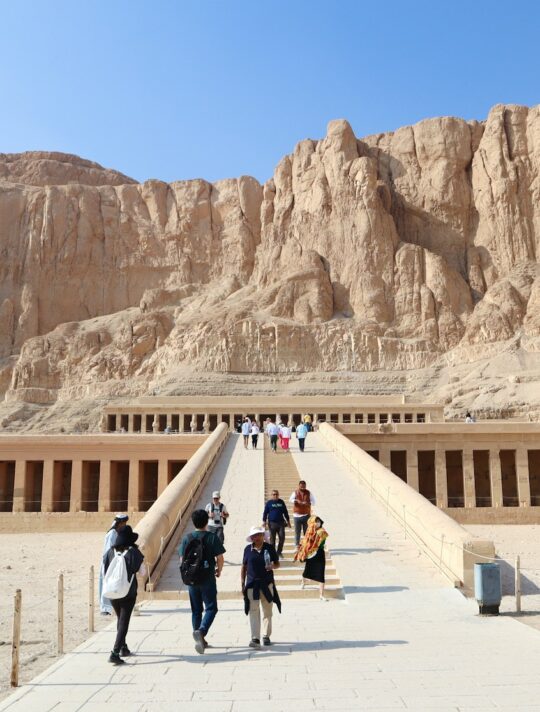 a group of people walking across a bridge in front of a mountain